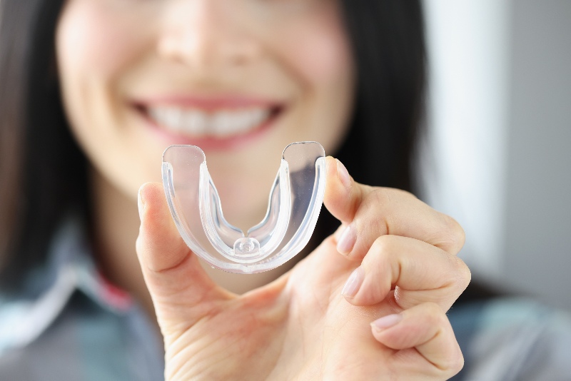 A Smiling woman holds a transparent plastic mouth guard in her hand